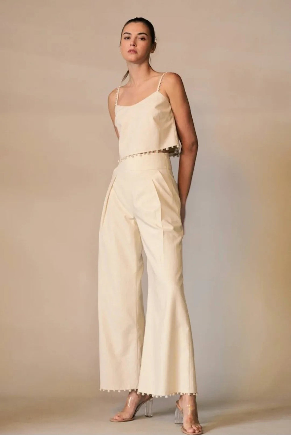 Model wearing a cream Shadow & Shine sleeveless crop top and wide-leg trousers with pom-pom trim detail.
